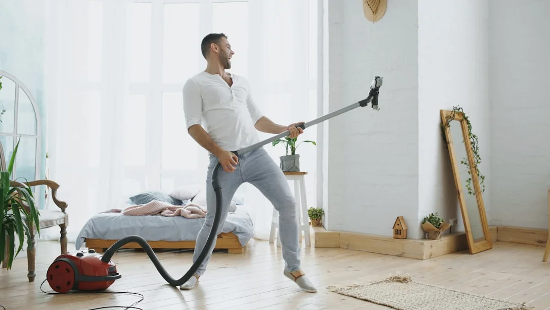 An individual is lifting a sofa in a minimalist living room with wooden flooring.